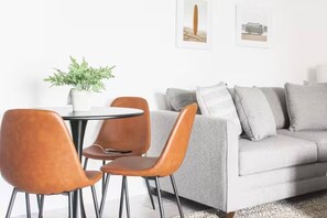 A modern living room with a grey sofa, two brown chairs, a small round table, and a potted plant.
