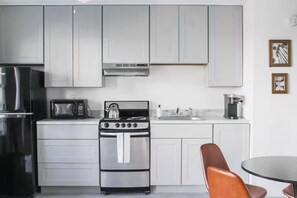 A modern kitchen with stainless steel appliances, white cabinetry, a coffee maker, and a dining area with a table and chairs.