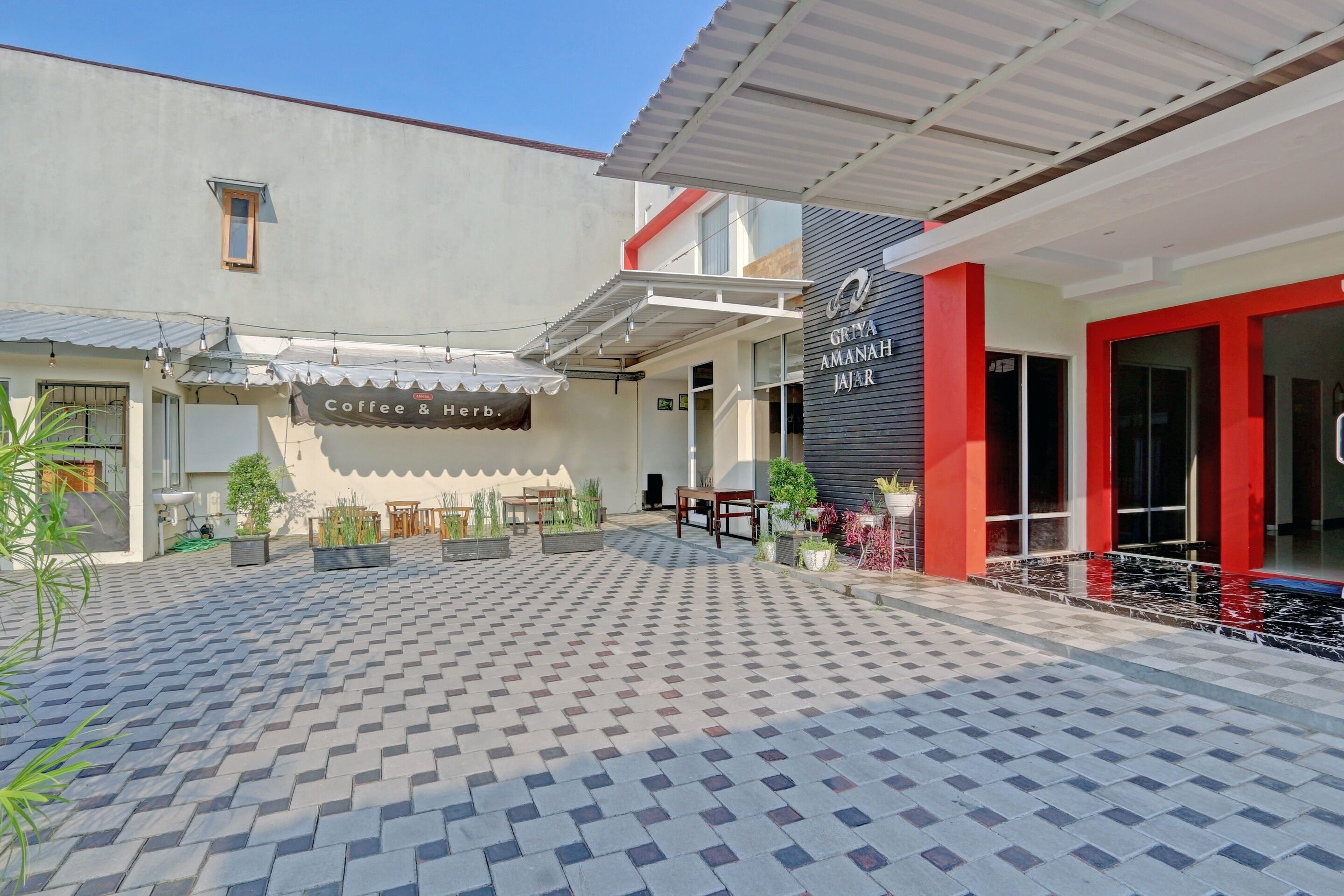 A courtyard with a coffee shop named 'Coffee & Herb' and a building with a sign 'GRYA AMANAH JAJAR'.