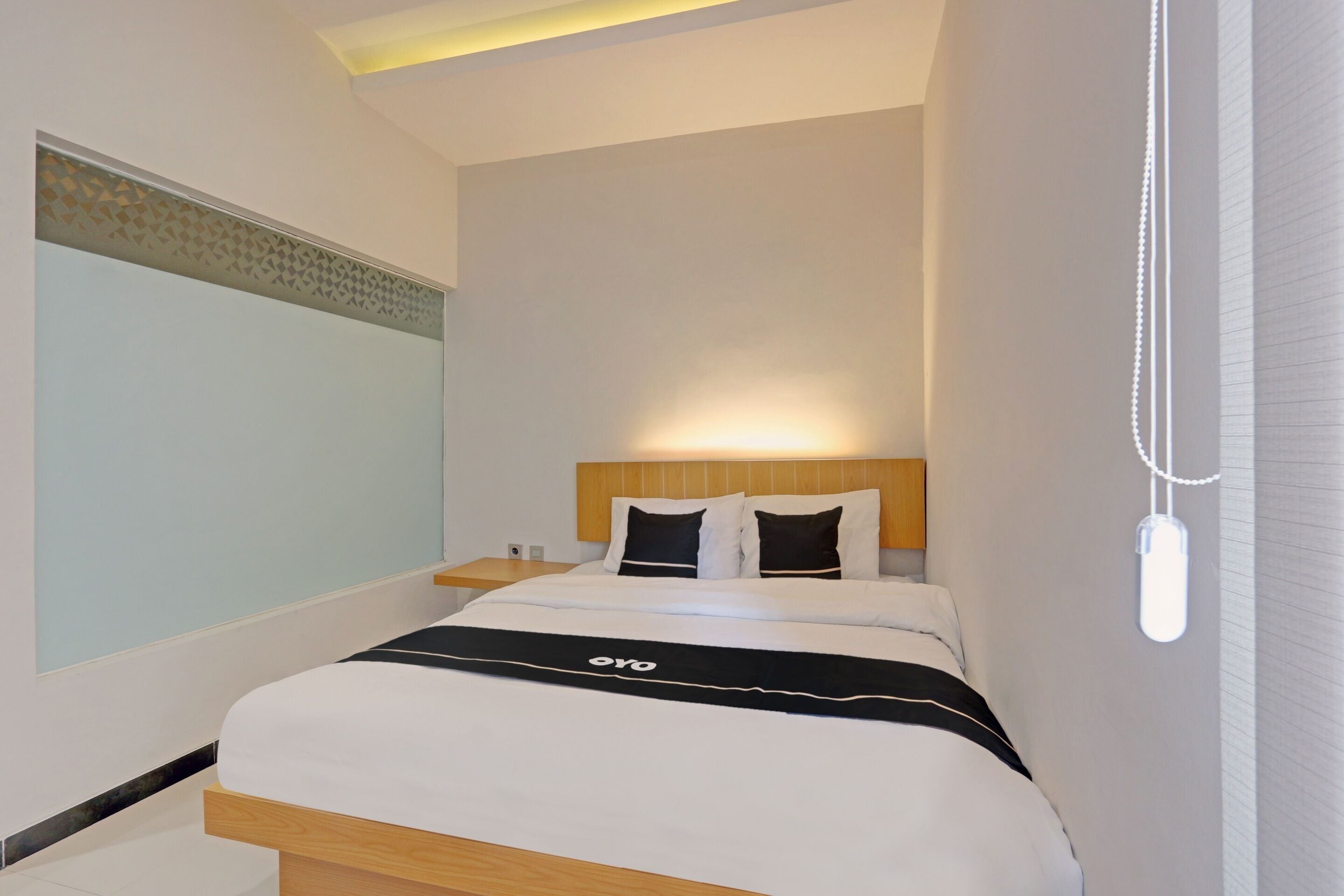 Une chambre d’hôtel moderne avec un lit bien fait, une table de chevet et un luminaire fixé au mur.
