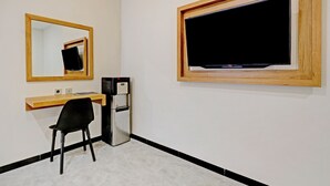 A small room with a wooden-framed TV, a desk with a chair, and a refrigerator.