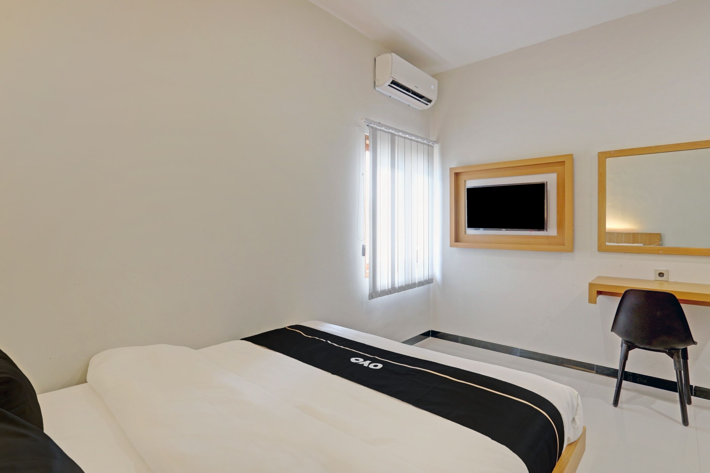 A hotel room with a bed, a desk, a chair, a TV, and an air conditioning unit.