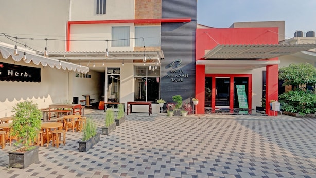 A modern building with a red and grey facade, a sign for 'GAYA AYANAH JYAR', and an outdoor seating area with tables and chairs.