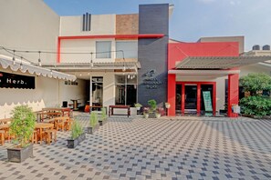 A modern building with a red and grey facade, a sign for 'GAYA AYANAH JYAR', and an outdoor seating area with tables and chairs. - OYO Capital O 90410 Griya Amanah Jajar Syariah (Surakarta)