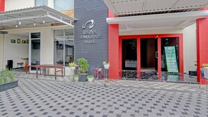A modern building with a grey and red facade, a covered outdoor seating area with tables and chairs, and potted plants.