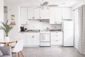 A modern kitchen with white cabinets, a ceiling fan, and a dining area with a table and chairs. - Central Location l Steps from Ocean l Top Floor (Myrtle Beach)