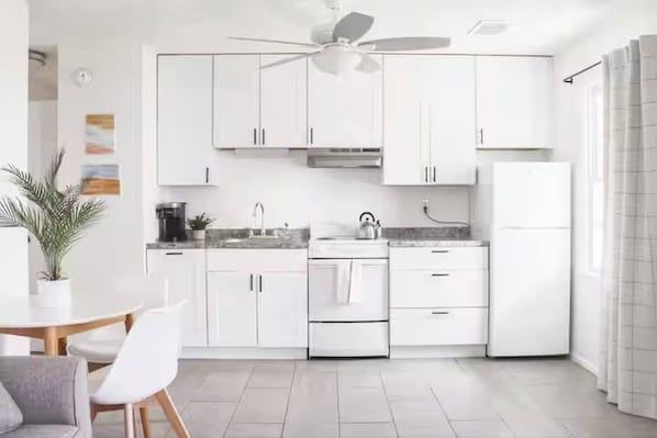 A modern kitchen with white cabinets, a ceiling fan, and a dining area with a table and chairs.