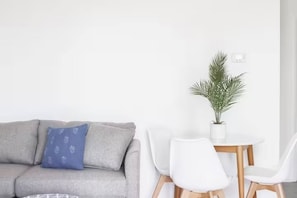 A room with a grey sofa, a small table with two white chairs, and a potted plant.