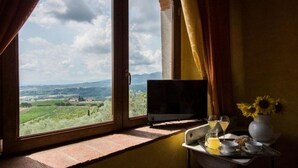 A room with a window overlooking a landscape, a small table with a vase of sunflowers, and a television on the windowsill.