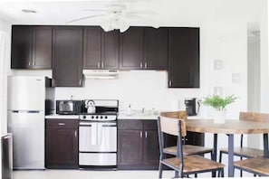 A modern kitchen with dark cabinets, a stainless steel refrigerator, a gas stove, and a dining table with chairs.
