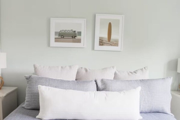 A bed with multiple pillows and two framed pictures on the wall above.