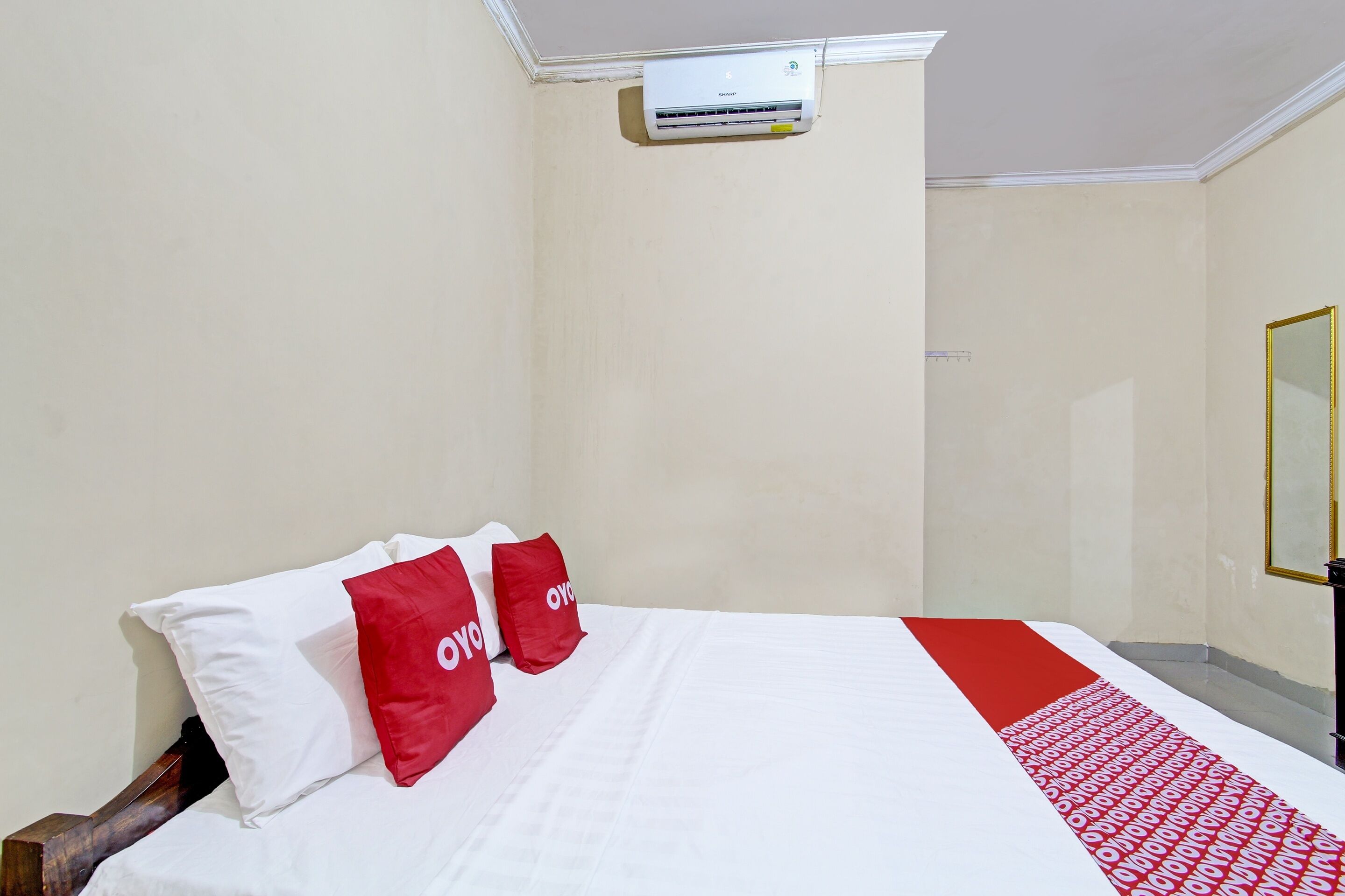 Une chambre d’hôtel avec un lit, des oreillers blancs et rouges, une couvre-lit rouge et blanche, et un appareil de climatisation fixé au mur.
