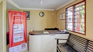 Un comptoir d’accueil avec une horloge, une fenêtre grillagée et une banderole rouge faisant la publicité d’un hôtel.
