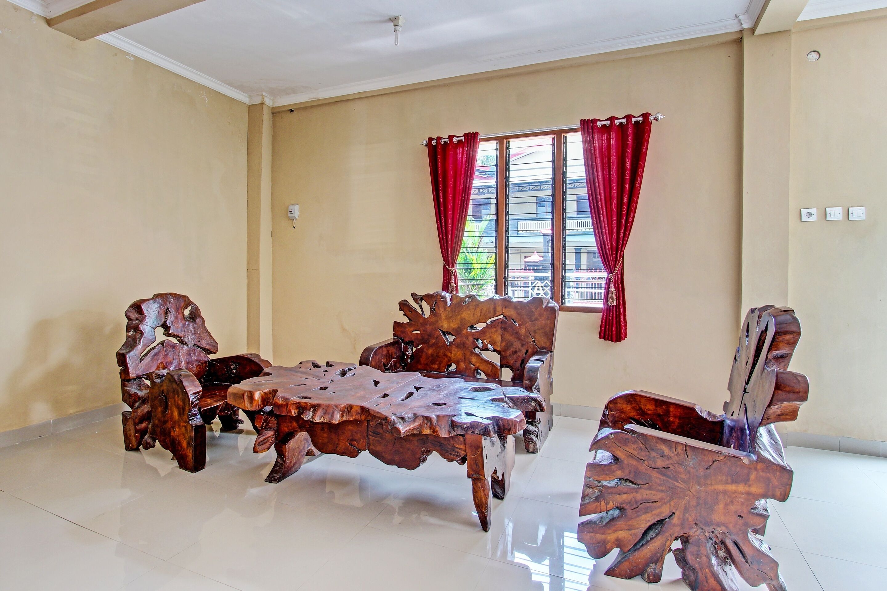 Une pièce avec une grande table et des chaises en bois, une fenêtre ornée de rideaux rouges et un mur de couleur beige.