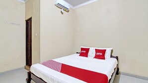 Un lit bien fait, avec une literie blanche et rouge, une tête de lit en bois et un plaid à motifs rouges et blancs.
