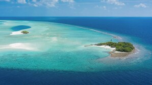 An aerial view of a tropical island with clear turquoise waters, a small sandy beach, and lush greenery. - FINS DIVE AND LEISURE HOTEL (Rasdhoo)