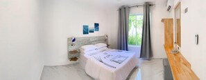 A bedroom with a bed, a window with curtains, a wooden dresser, and a wall-mounted air conditioning unit. - FINS DIVE AND LEISURE HOTEL (Rasdhoo)