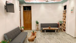 A modern hotel lobby with a grey sofa, a wooden coffee table, and a television mounted on the wall. - FINS DIVE AND LEISURE HOTEL (Rasdhoo)