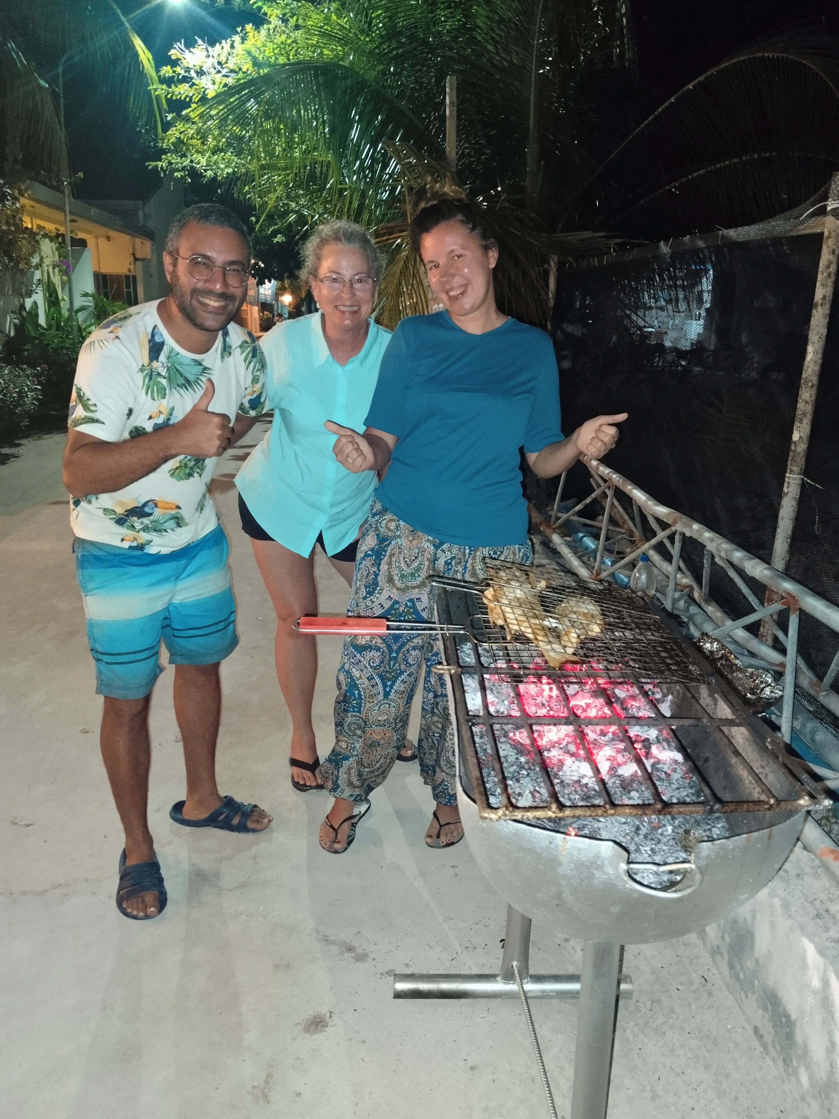 Drei Personen stehen in der Nähe eines Grills, auf dem Essen zubereitet wird.