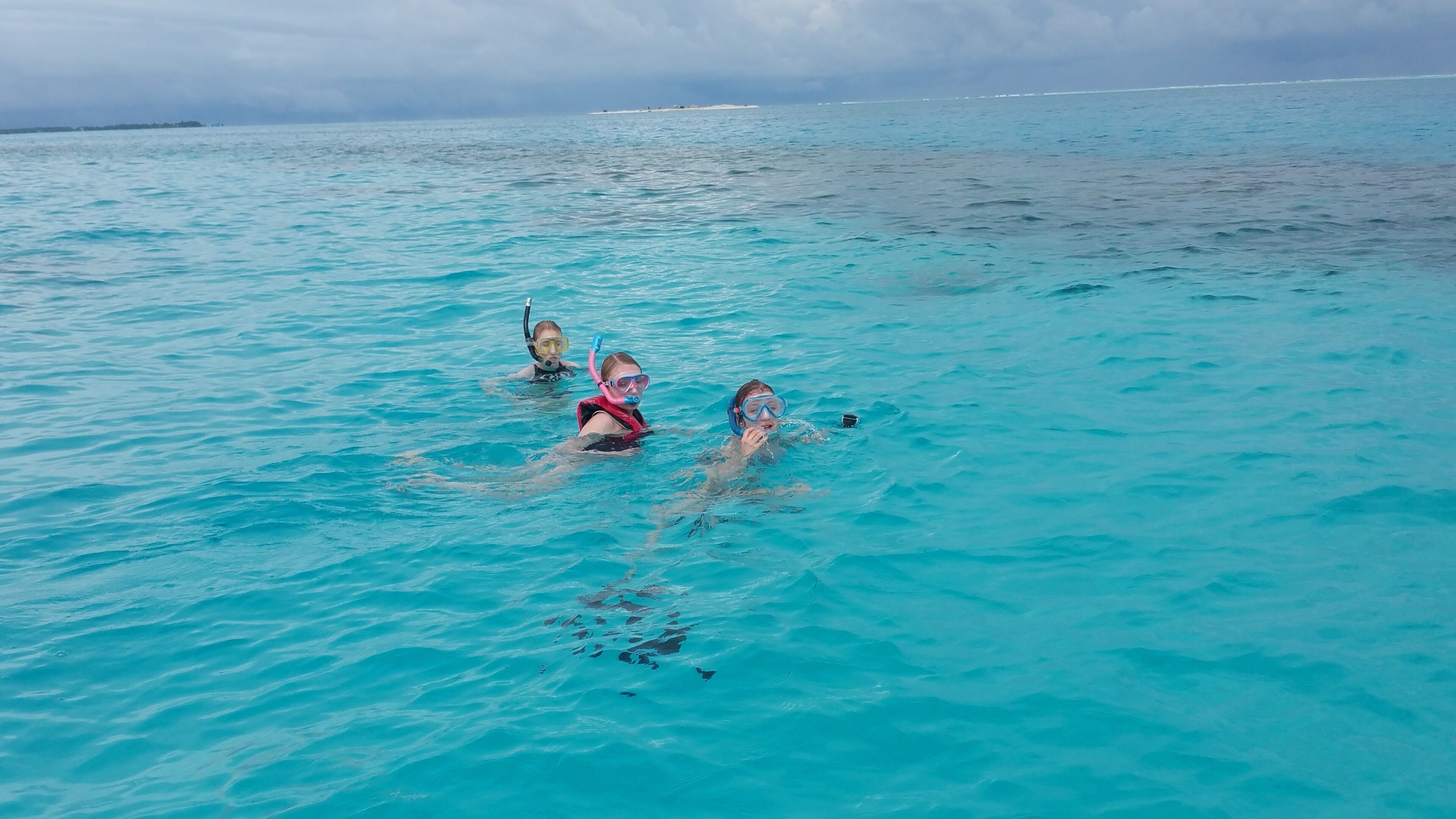 Trois personnes font de la plongée avec tuba dans une eau turquoise et cristalline.