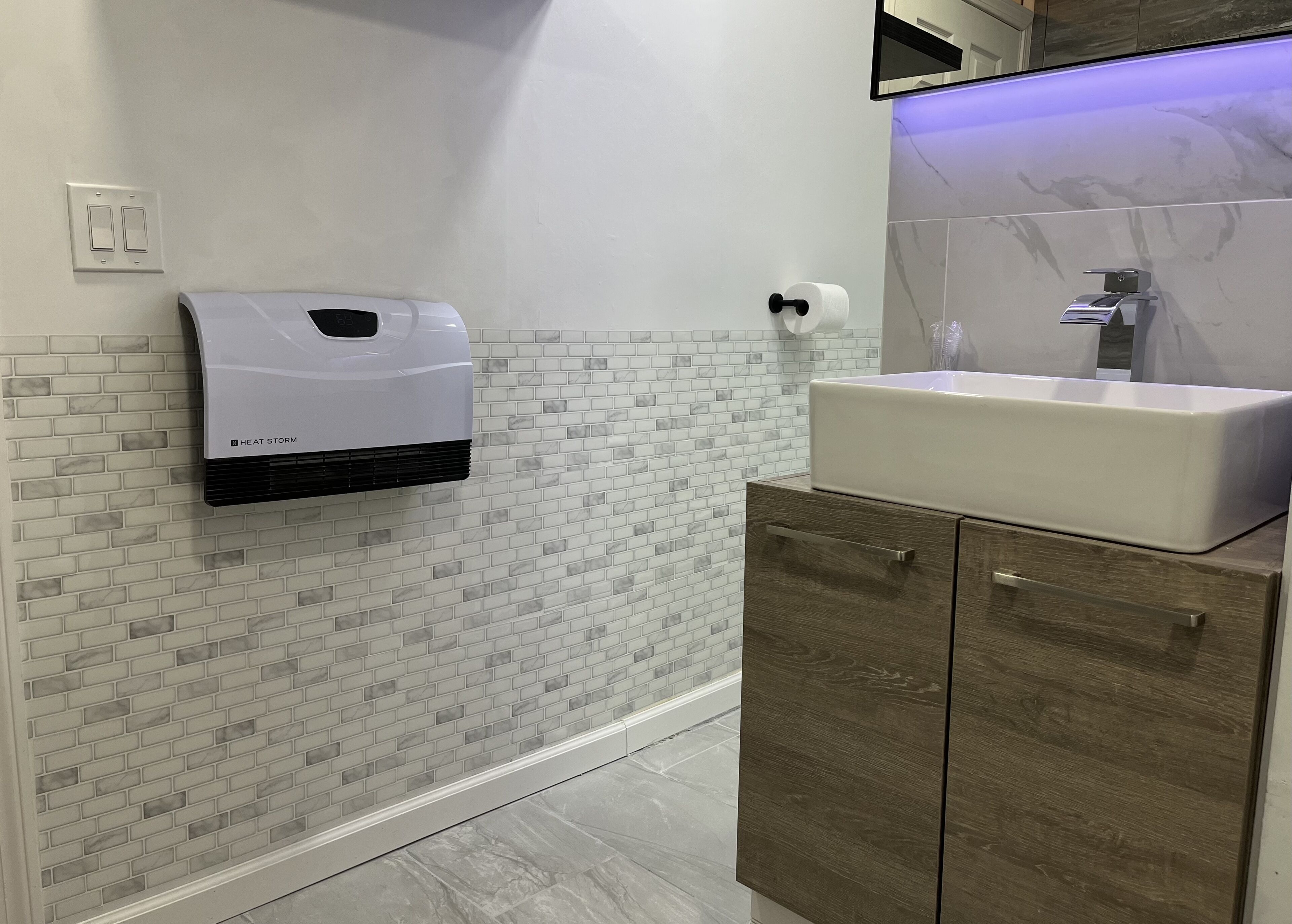 Une salle de bain avec un lavabo blanc, un distributeur de serviettes en papier fixé au mur et un miroir au-dessus du lavabo.