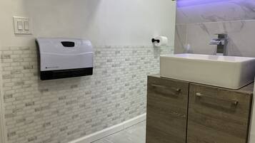 Une salle de bain avec un lavabo blanc, un distributeur de serviettes en papier fixé au mur et un miroir au-dessus du lavabo.