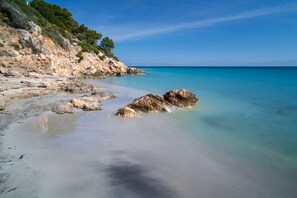 Ein Küstenstrand mit felsigem Gelände und klarem, blauem Wasser.