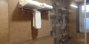 A bathroom with a towel rack, a shower area, and a patterned tile wall. - Candolim Suites (Candolim)
