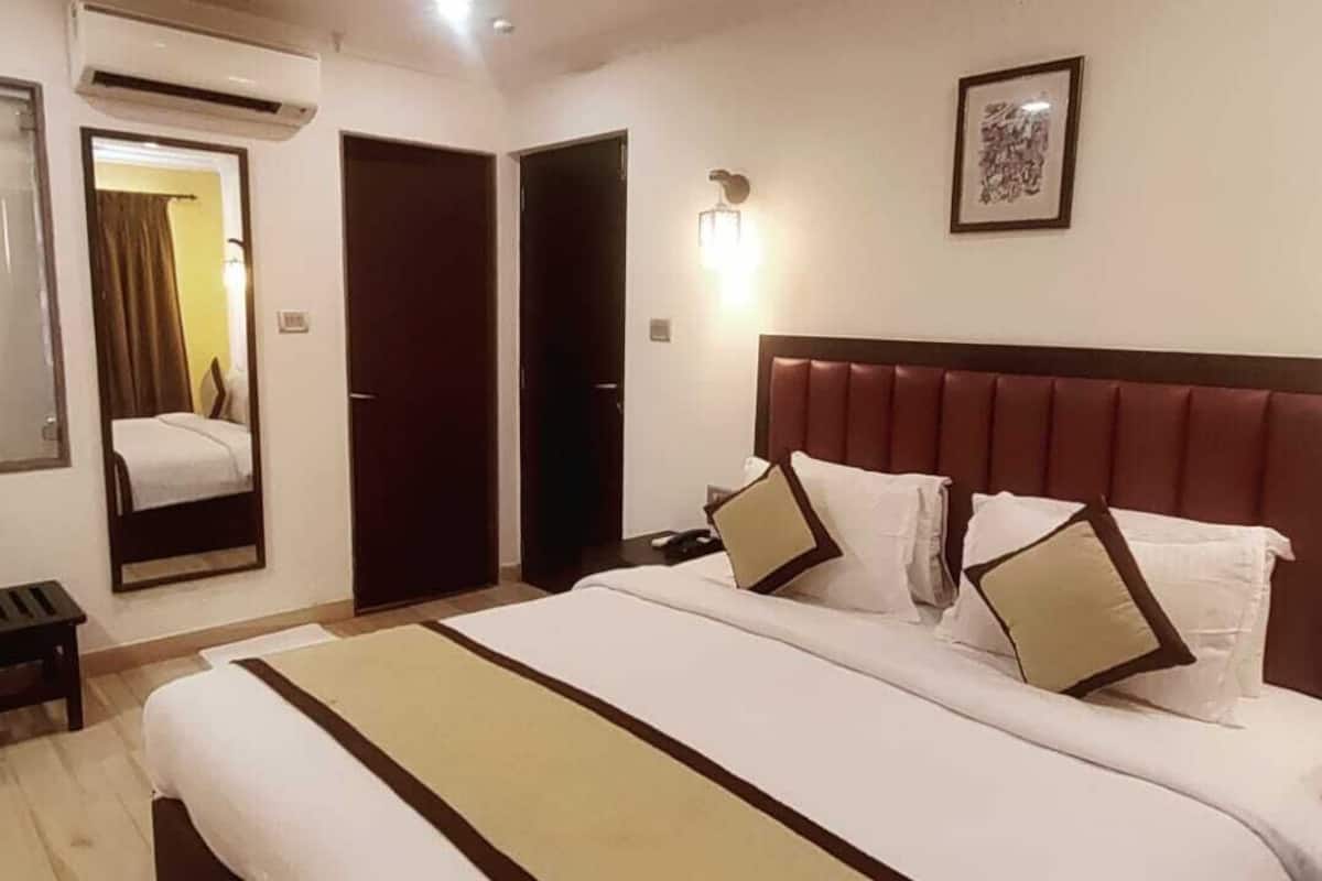 A hotel room with a large bed, a bench, a mirror, and a door.
