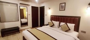 A hotel room with a large bed, a bench, a mirror, and a door. - Candolim Suites (Candolim)