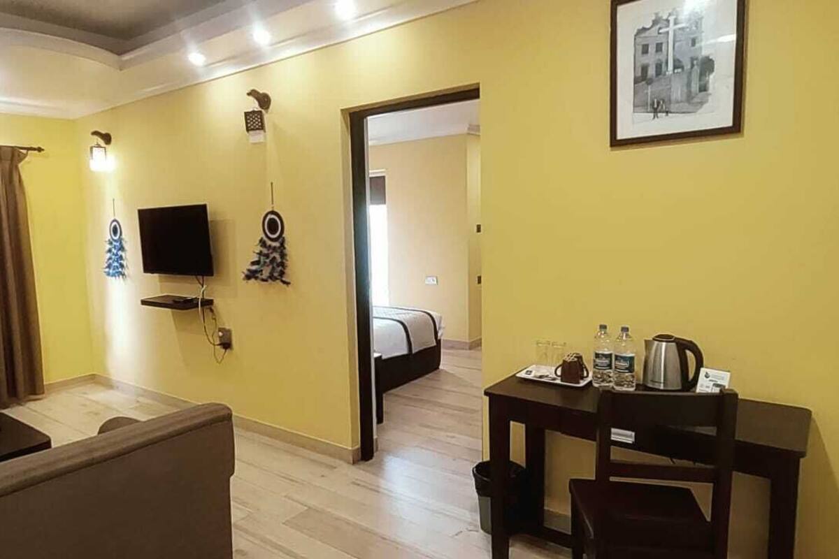 A hotel room with a sofa, a TV, a small table with a kettle, and a framed picture on the wall.