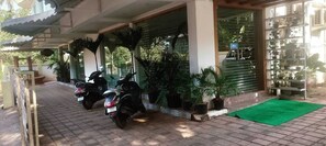 A covered parking area with two scooters parked, surrounded by potted plants and a green mat. - Candolim Suites (Candolim)