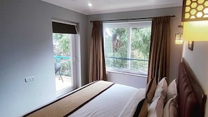 A hotel room with a bed, a window with curtains, a balcony, and a wall-mounted light fixture. - Candolim Suites (Candolim)