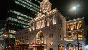 Een historisch gebouw met een opvallende koepel en 'Hamilton' bord, omringd door moderne wolkenkrabbers.