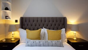 Een net opgemaakt bed met een gestoffeerd hoofdbord, twee bedlampen en een nachtkastje met een kleine vaas.