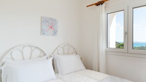 Ein Schlafzimmer mit einem Bett, weißen Vorhängen, einem Fenster mit Aussicht und einem an der Wand hängenden Kunstwerk.