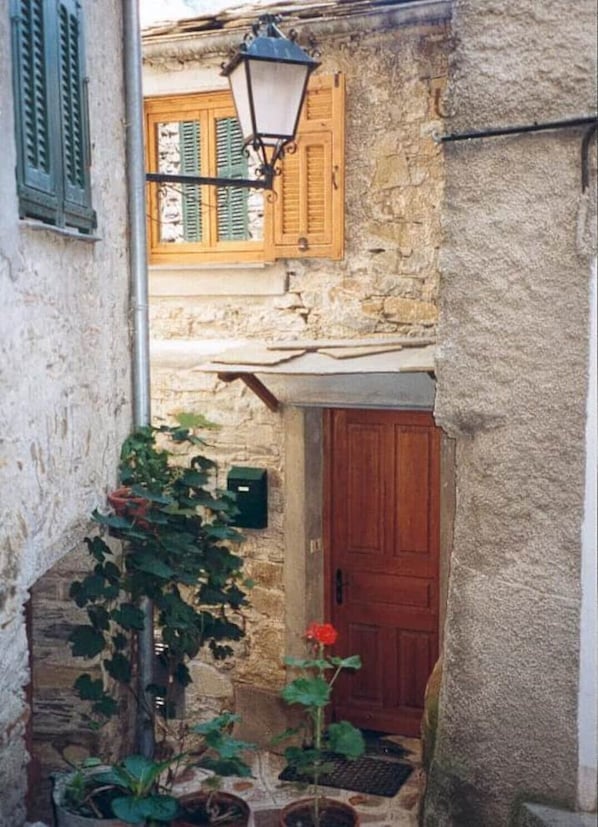 Un carreró estret amb una porta de fusta i un fanal penjant. Hi ha plantes en testos i un petit escaló que mena a la porta.