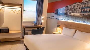 Quarto de hotel com cama, escrivaninha, cadeira e vista para o mar através de uma janela.