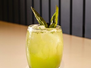 Un verre contenant une boisson verte, des feuilles de menthe et des glaçons, le tout sur un fond sombre.