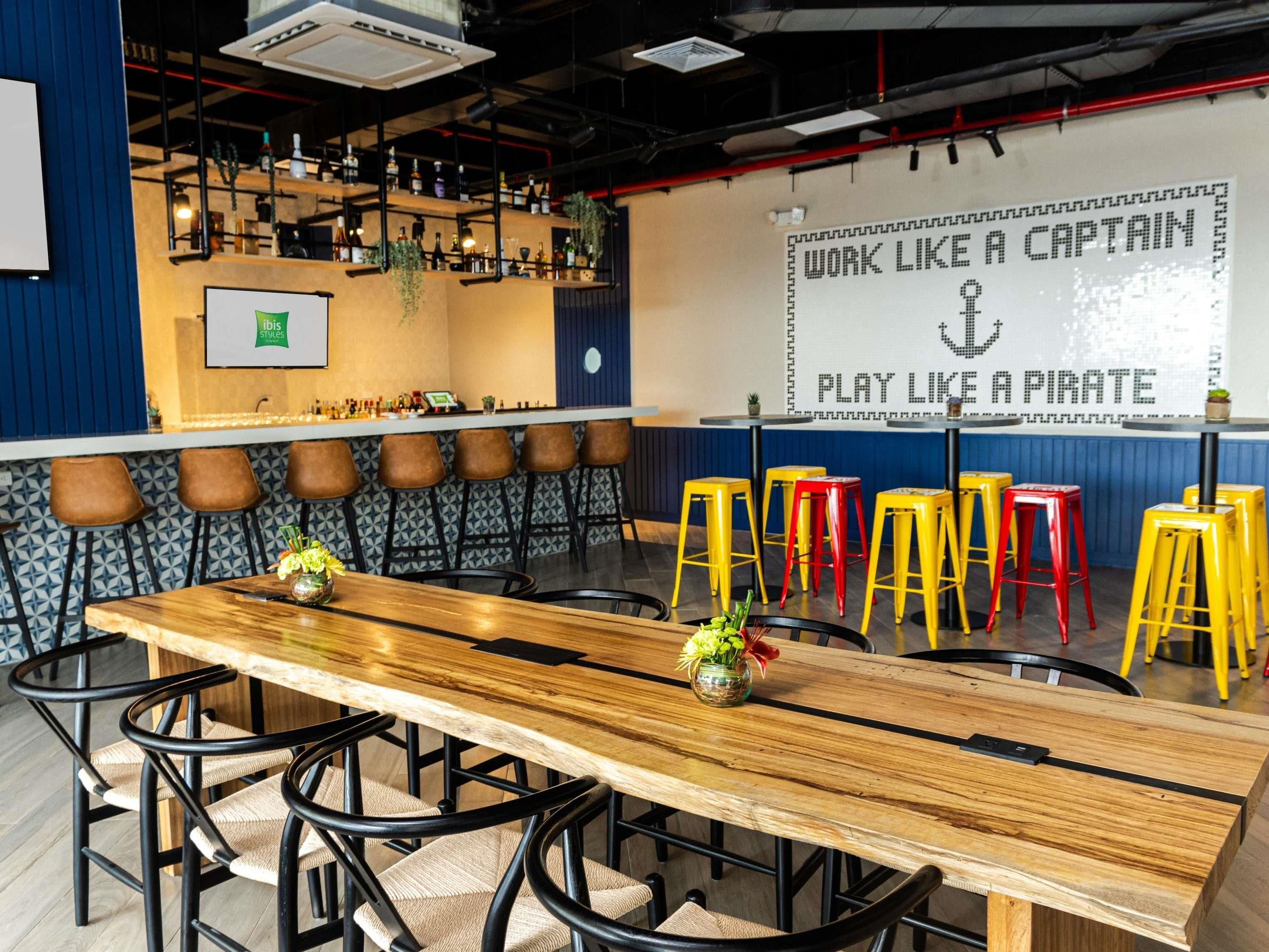 Una zona de bar con una larga mesa de madera, varios taburetes y una pared decorada con frases motivacionales.