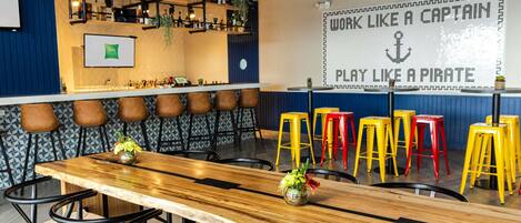 Una zona de bar con una larga mesa de madera, varios taburetes y una pared decorada con frases motivacionales.