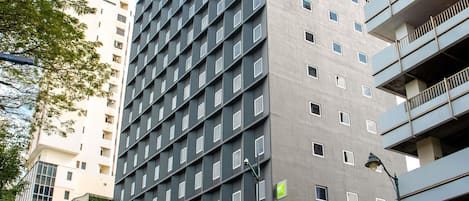 A multi-story building with a grid of windows, a green sign, and a street lamp.