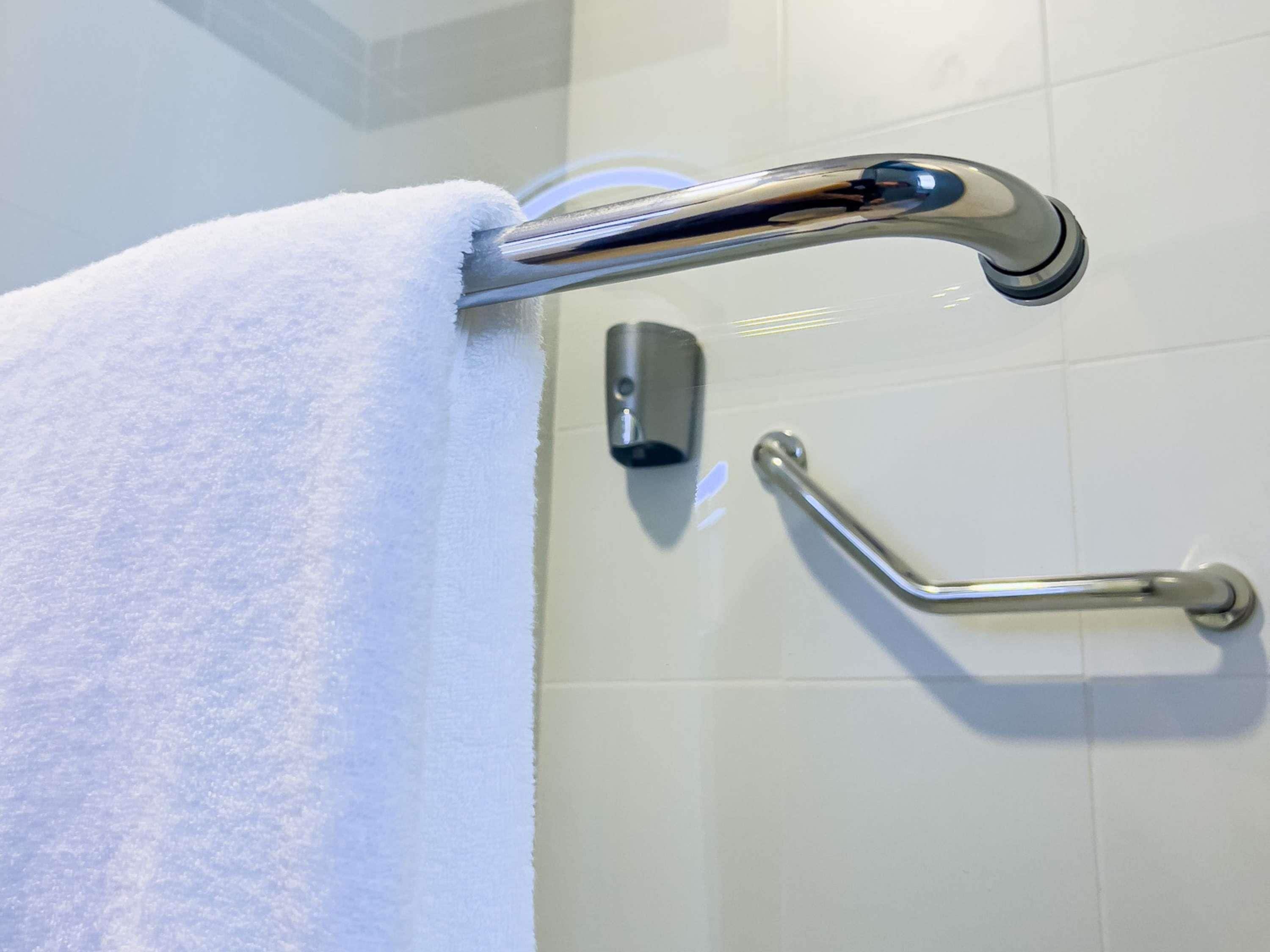 A bathroom with a white towel hanging on a chrome towel bar, a hand dryer, and a grab bar on the wall.