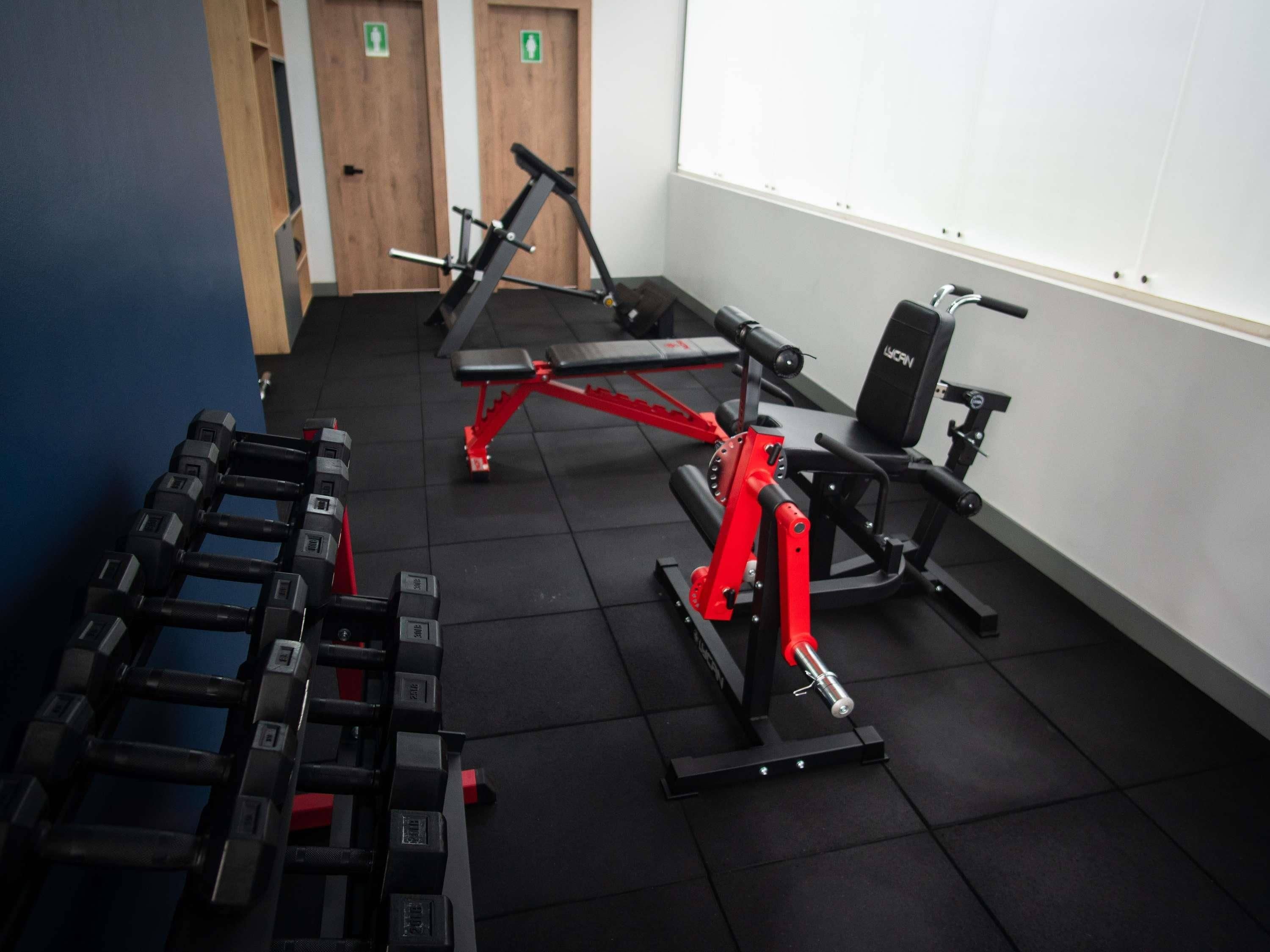 Une salle de sport équipée de matériel d’exercice, notamment des haltères, un banc et une machine rouge.
