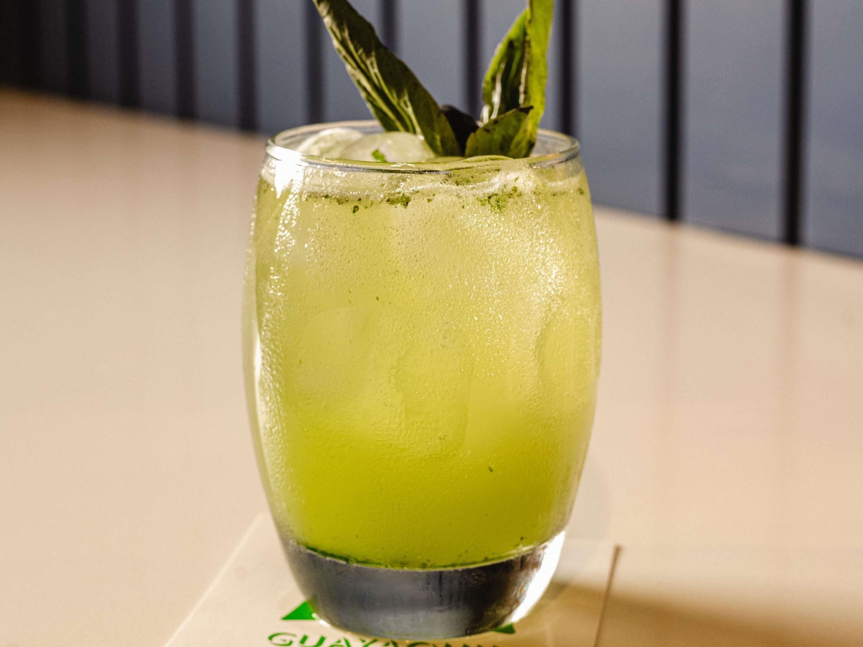 Un verre d’une boisson verte, garnie de feuilles de menthe, posé sur une table ornée d’un logo.