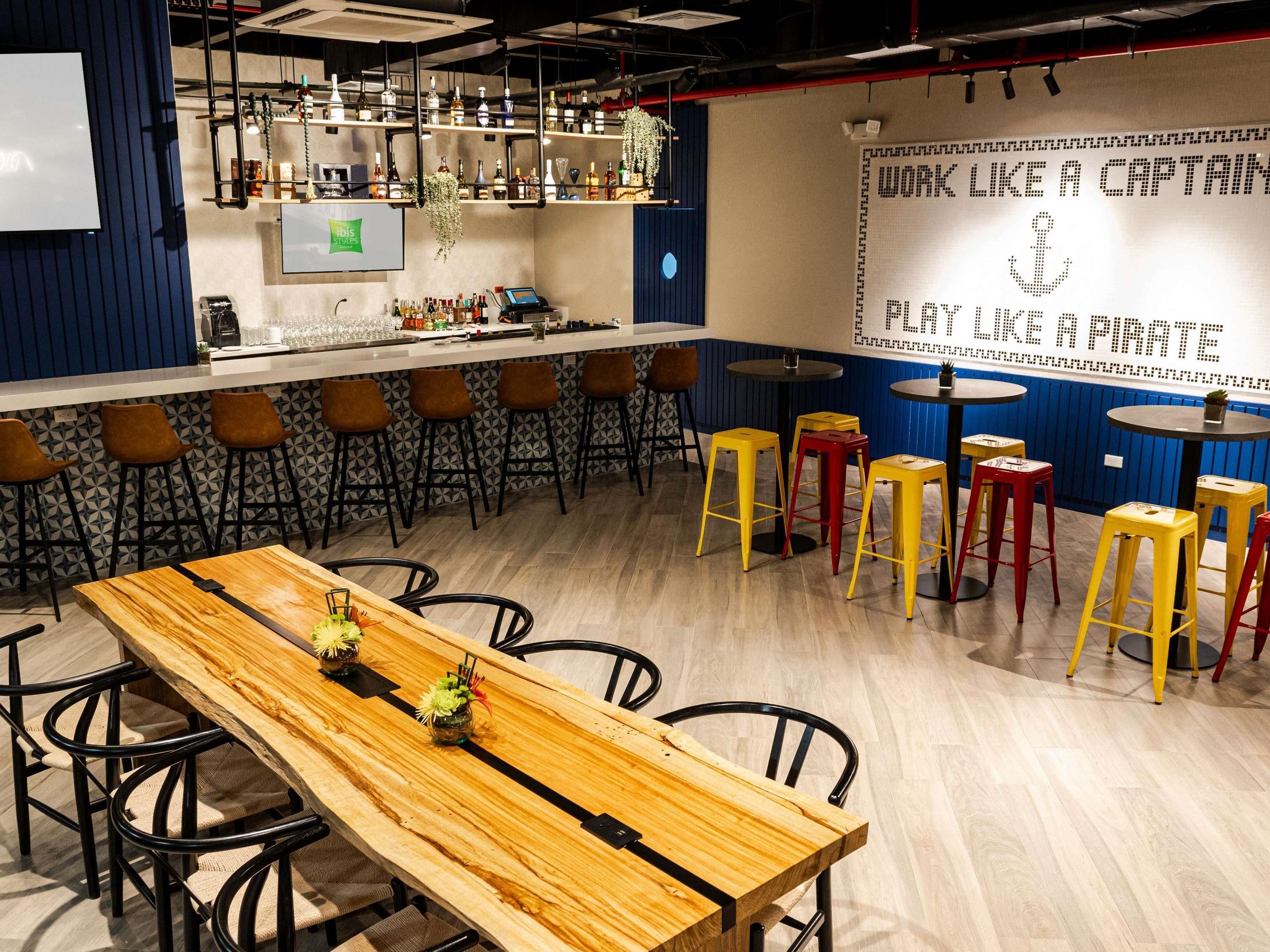 A bar area with a long wooden table, multiple stools, and a bar counter with shelves of bottles.