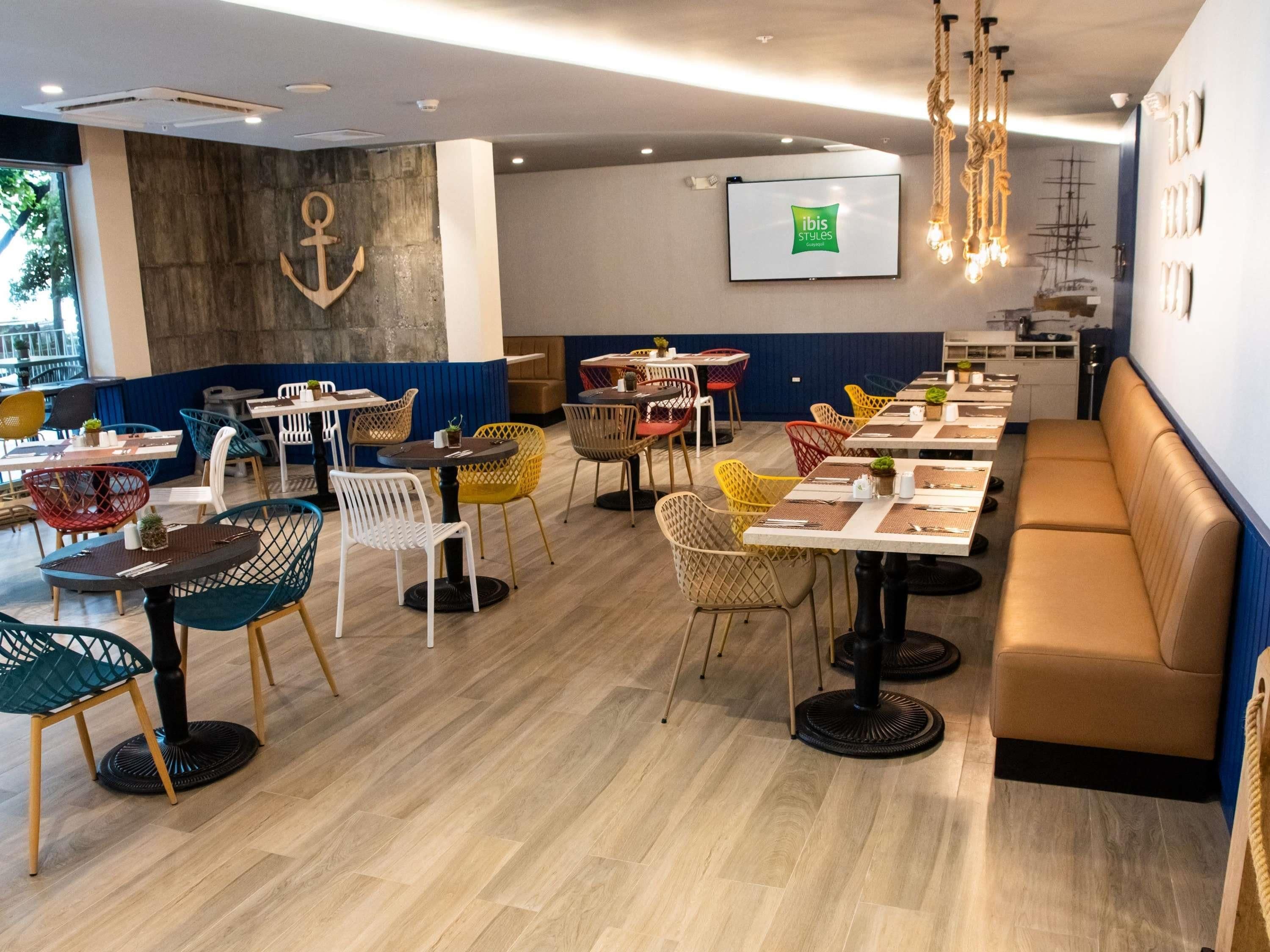 Een restaurant in nautische stijl, met ankerdecoratie, houten vloeren en diverse kleurrijke stoelen en tafels.