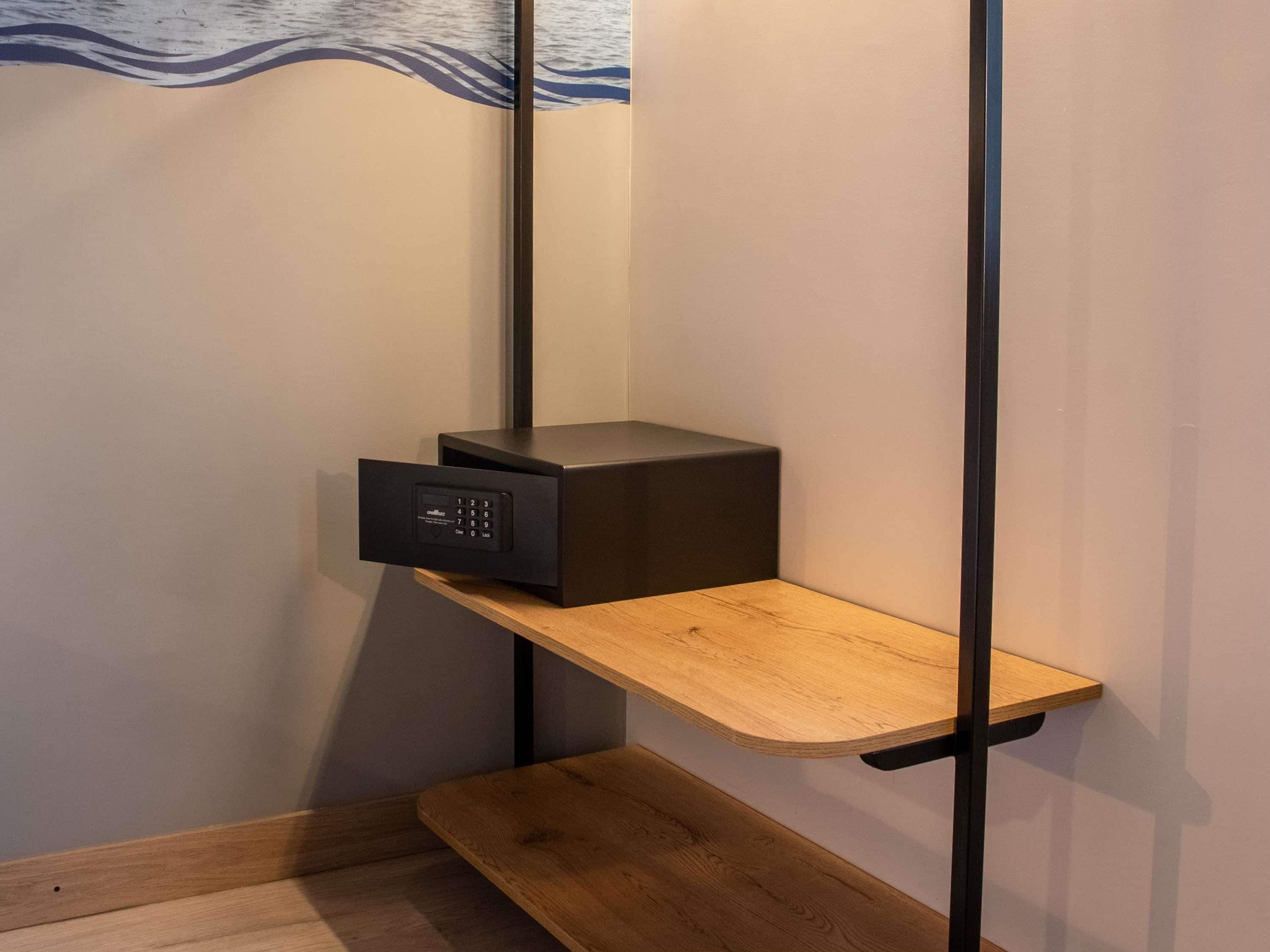 A corner of a room with a wooden shelf, a black electronic device, and a wall with a wave pattern.
