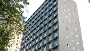 Un hotel moderno de altura con fachada uniforme, varios balcones y una entrada a nivel de la calle.