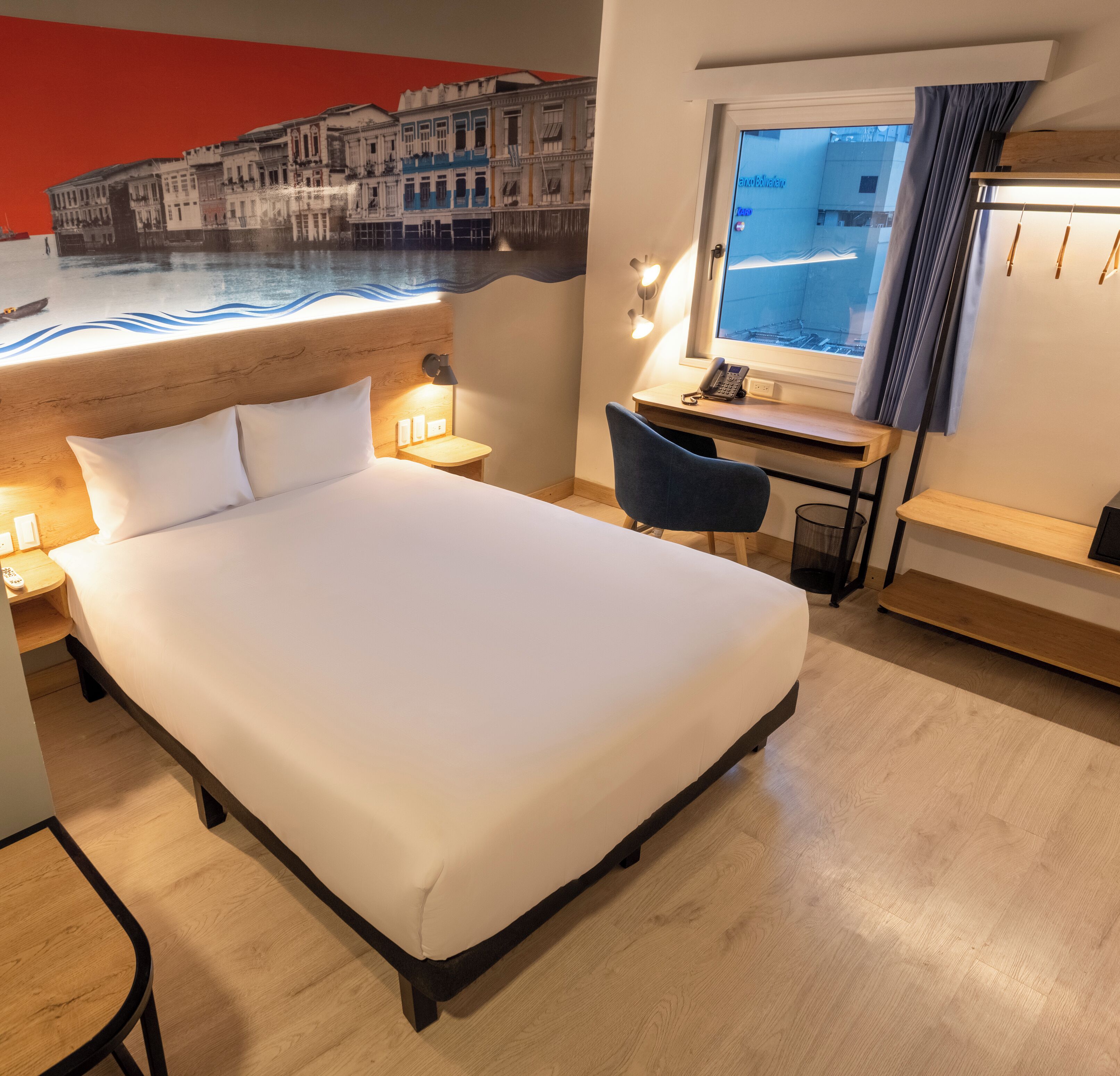 Habitación de hotel con cama, escritorio, silla y vistas a la ciudad por la ventana.